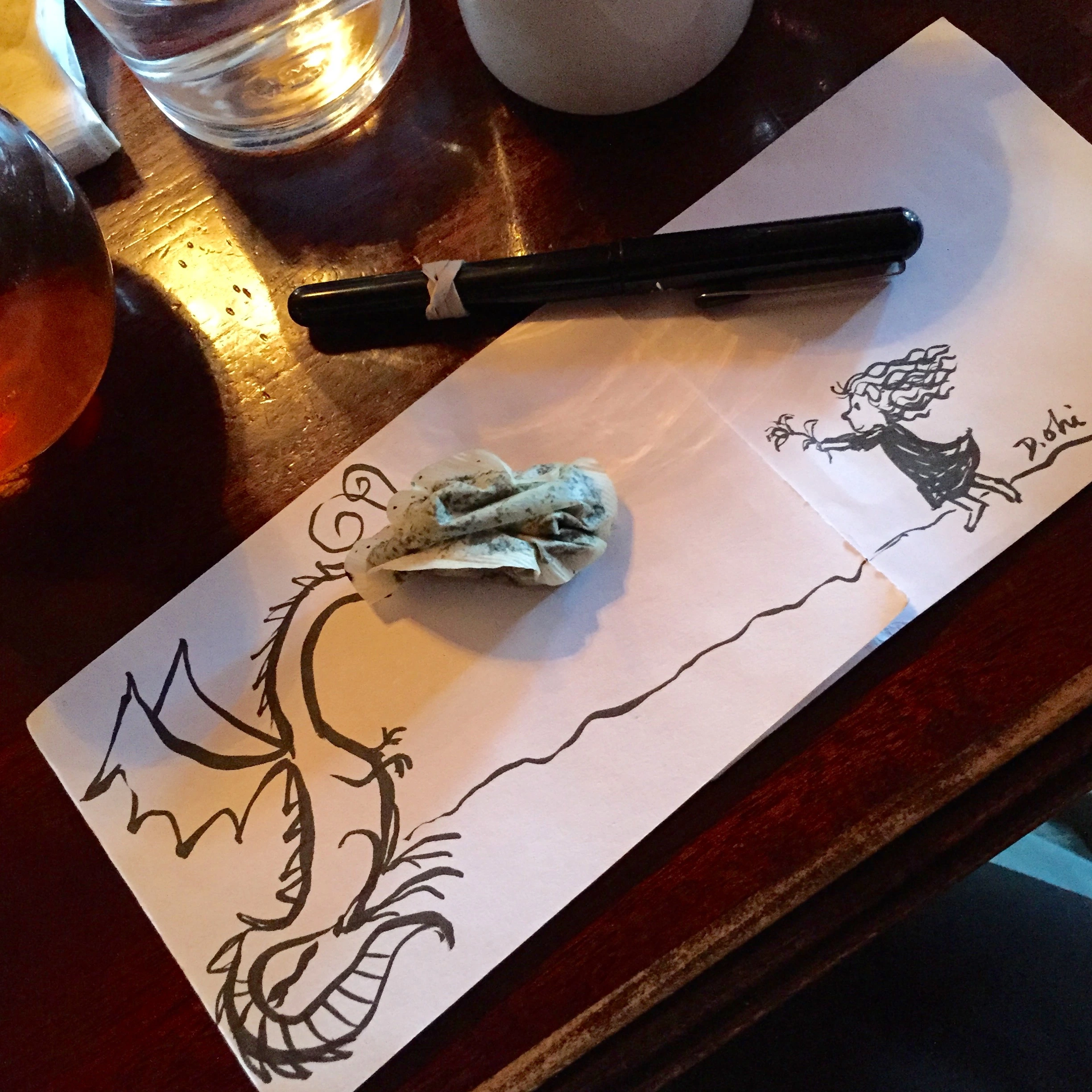 Found object art featuring tea bag dragon head looking at a drawing of a small girl holding up a flower